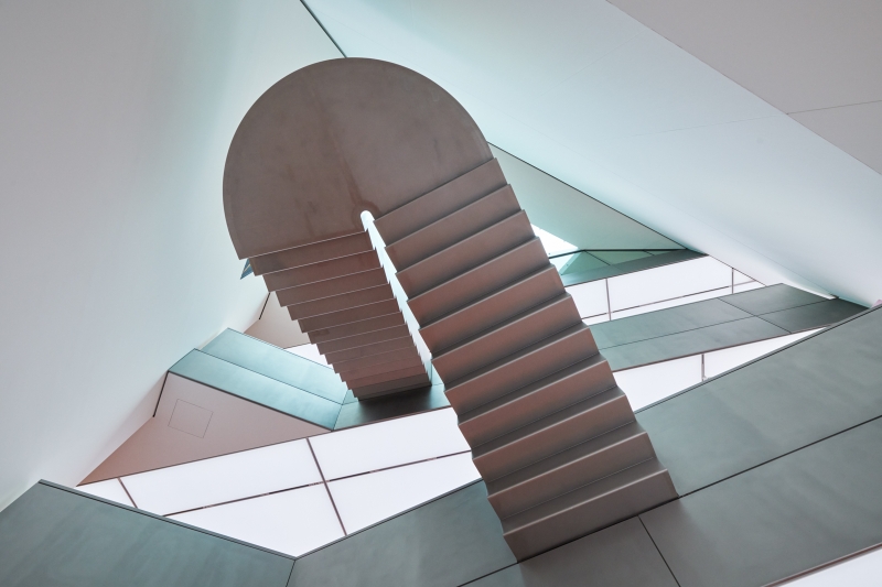 Abstract architectural design featuring a curved staircase against angular walls and large windows.