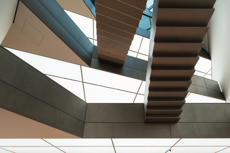 Geometric staircase design with angular lines and contrasting materials, illuminated by soft, diffused lighting.