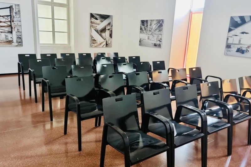A row of black plastic chairs arranged in a bright room with large windows and art on the walls.