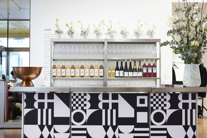 A modern bar with geometric black and white patterns, glassware, and bottles of wine, adorned with floral arrangements.
