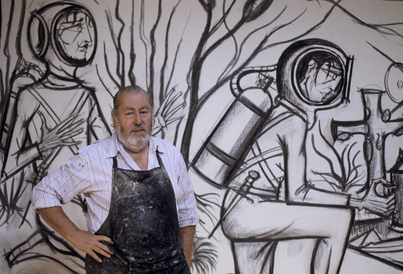 Mann mit Bart in Atelier, vor einer Wandzeichnung von Taucherfiguren und Pflanzen.