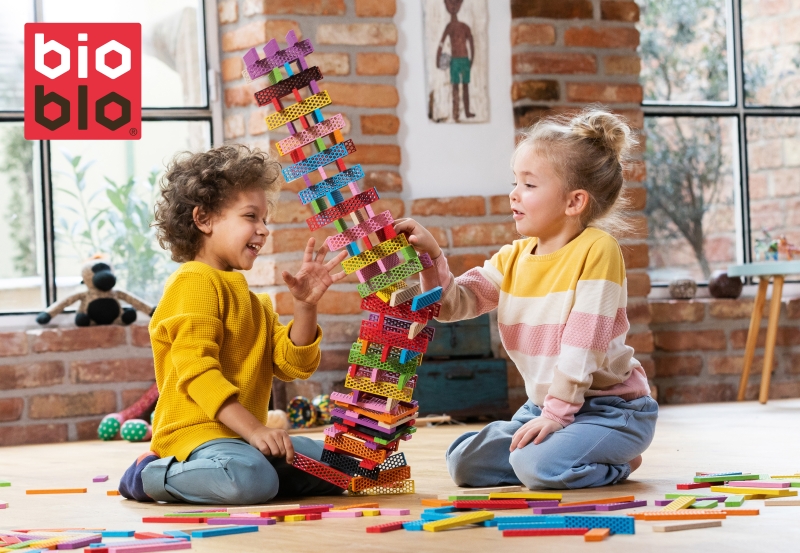 Ein M&auml;dchen und ein Junge bauen einen Turm aus bunten Bioblo Steinen