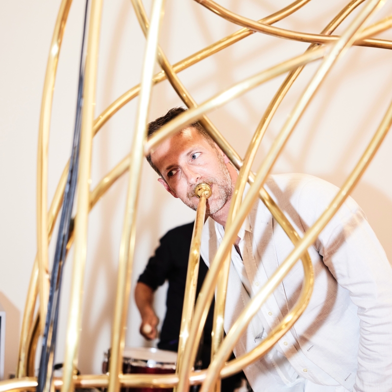 Mann mit Trompete zwischen goldenen Skulpturen, im Hintergrund ein Schlagzeuger.