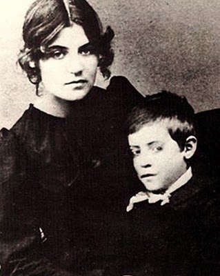 Suzanne Valadon sitzt mit ihrem Sohn Maurice Utrillo, beide in historischen Kleidern, ernst blickend in die Kamera.