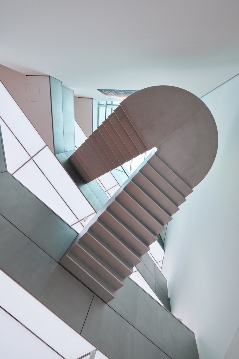 The picture shows a floating staircase inside the Heidi Horten Collection in Vienna.
It connects two floors of the museum.

The walls and ceilings are white and modern in design.
There are large windows through which daylight enters.
Everything looks bright, calm and clear.