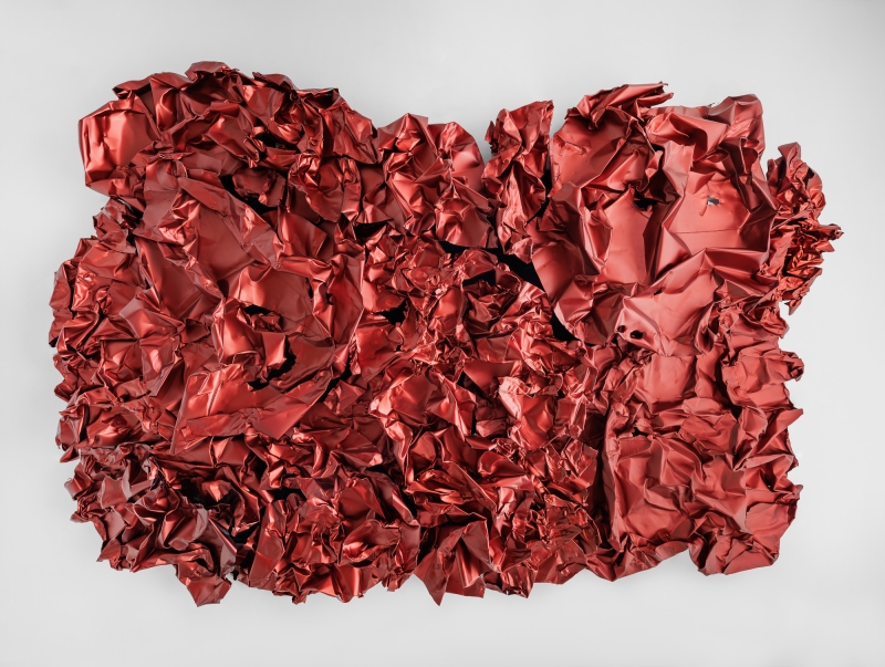 This work of art is by Hans Kupelwieser.
It is a large red wall relief made of aluminum.
The material has been crumpled and shaped,
so that it looks like crumpled wrapping paper or a giant red foil.
The surface is not smooth, but wrinkled and full of dents and holes.
It looks as if it was created by chance, but it is precisely planned.
Kupelwieser uses machines and gripper excavators to deform the aluminum.
The red color comes from a chemical process called anodizing.
This makes the metal look matt and soft - although it is actually hard.
The artwork hangs from the ceiling of the Tea Room in the Heidi Horten Collection museum in Vienna.
Kupelwieser plays with contrasts here:
light and heavy, soft and hard, coincidence and planning.