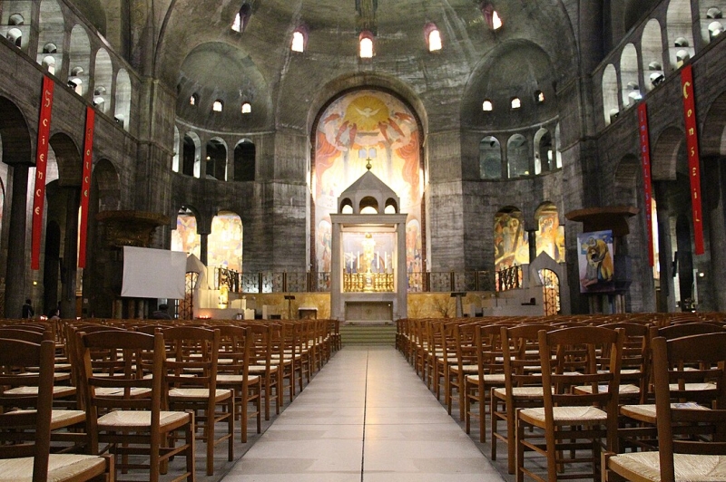 Innenansicht der &Eacute;glise du Saint-Esprit mit Holzst&uuml;hlen, bunten Wandmalereien und einem Altar im Hintergrund.