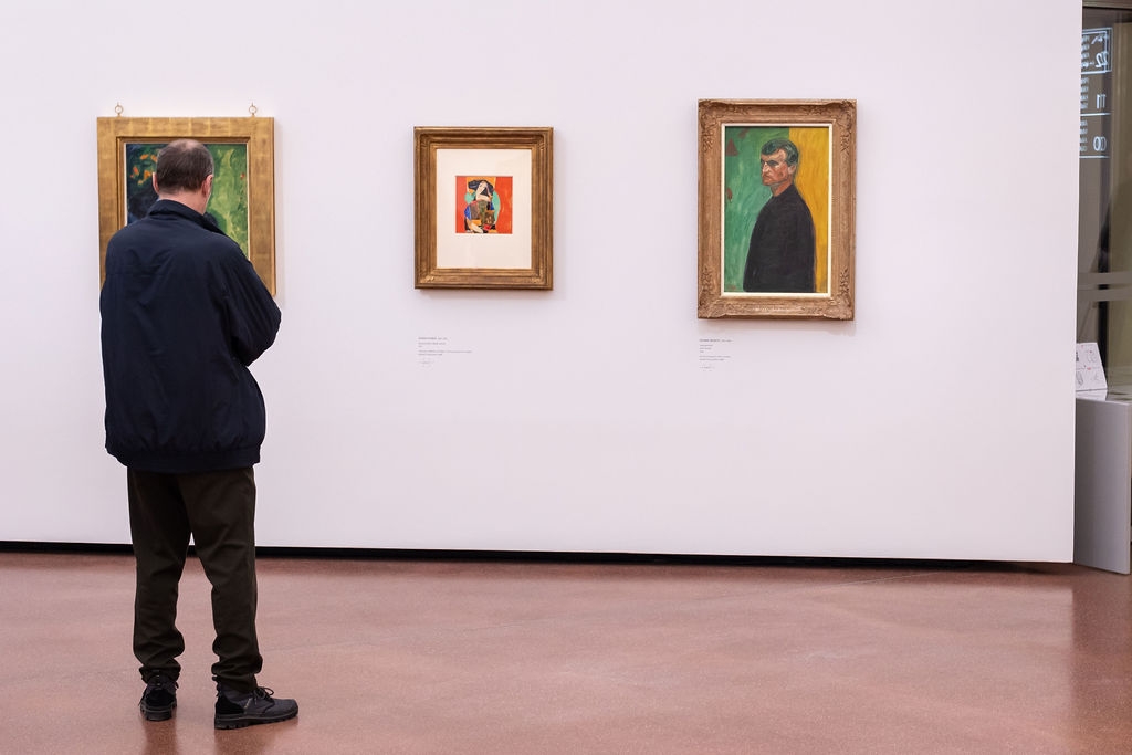Mann betrachtet zwei Gem&auml;lde in einem modernen Ausstellungsraum mit wei&szlig;en W&auml;nden und glattem Boden.