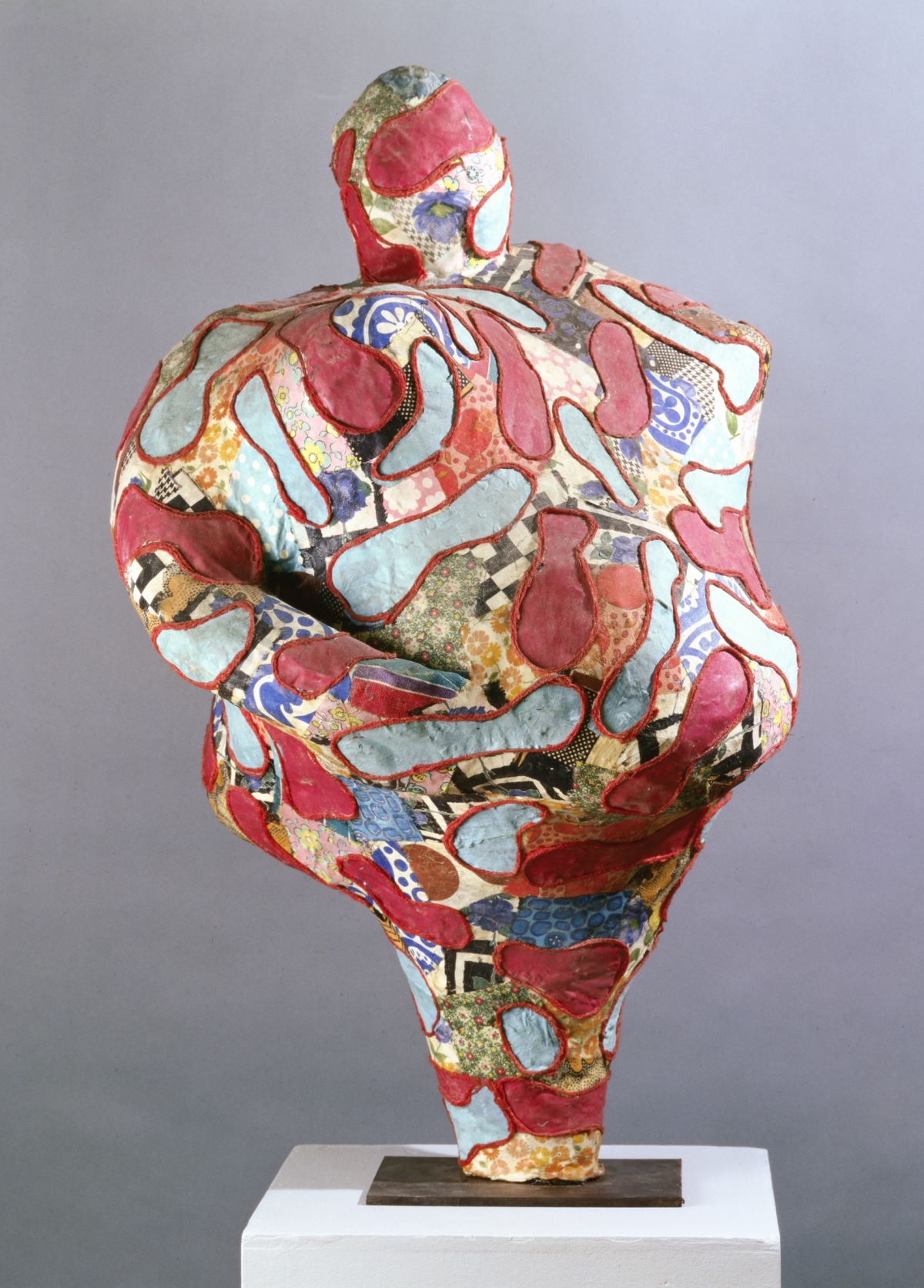 Skulptur in organischer Form, bunt mit roten, blauen und gemusterten Fl&auml;chen, auf einem wei&szlig;en Sockel pr&auml;sentiert.