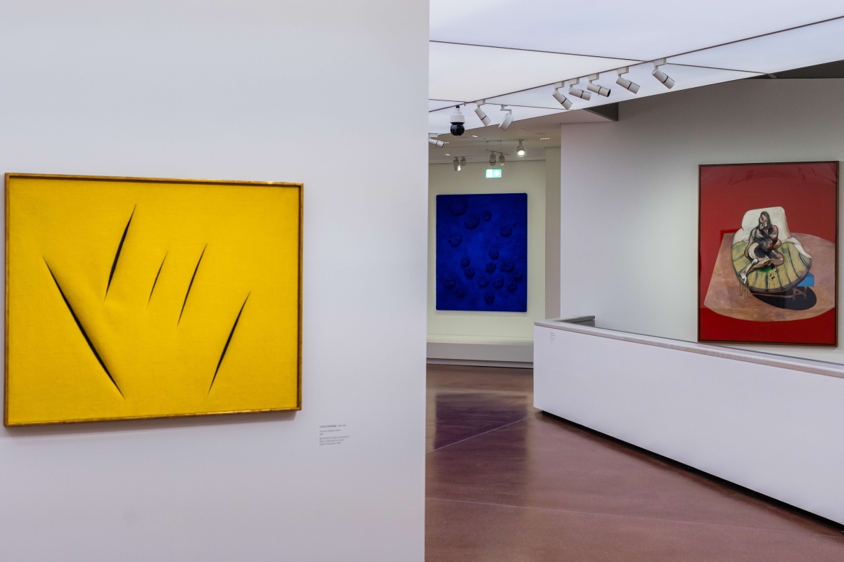 Gelbes Kunstwerk mit scharfen Einschnitten links, daneben blaue und rote Gemälde in moderner Galerie.