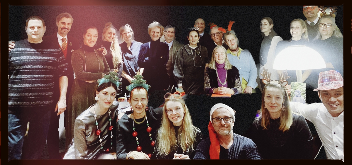 Gruppenszene mit 20 Personen in festlicher Kleidung und Weihnachtsaccessoires, fr&ouml;hliche Stimmung, dunkler Hintergrund.