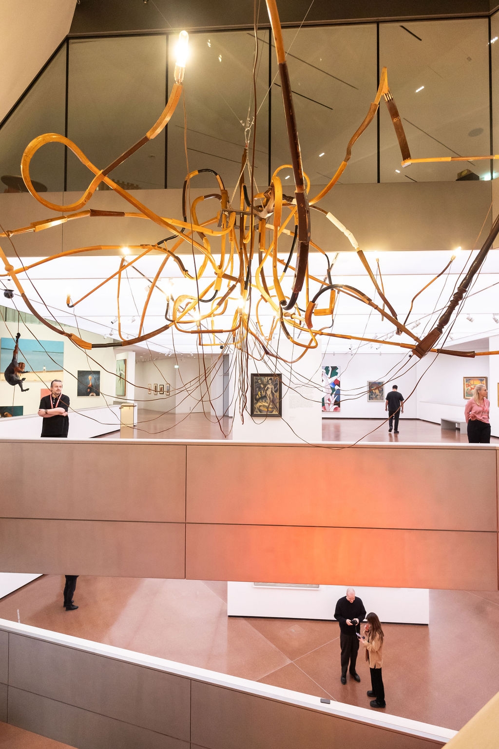 Moderne Galerie mit einer kunstvollen Deckeninstallation und Besuchern, die Gem&auml;lde betrachten.