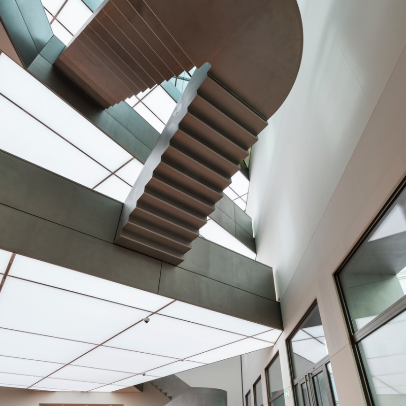 Modern interior featuring a sculptural staircase, large windows, and a bright, airy atmosphere with polished wooden floors.