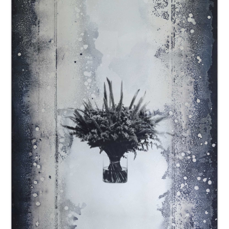 In the picture we see a mirror with a bunch of flowers in the middle.
The edges are dark and speckled, like an old photo or film.

The work of art is by Andreas Duscha.
He made the mirror himself, following an old recipe from the 17th century.
In the middle you can see an arrangement of flowers - it is a screen print on the mirror surface.

The flowers on the mirror have a deeper meaning:
They stand for social crises and revolutions.
A bouquet is a reminder of revolutions, for example: the Carnation Revolution in Portugal or
the Tulip Revolution in Ukraine.

Duscha is interested in hidden stories and connections.
He uses old techniques and special materials,
to make themes such as power, change and history visible in a quiet, poetic way.

This artwork is part of a series of four mirrors,
, which hang in the anteroom of the Heidi Horten Collection museum toilets.
Each mirror tells its own story - through plants and symbols.
