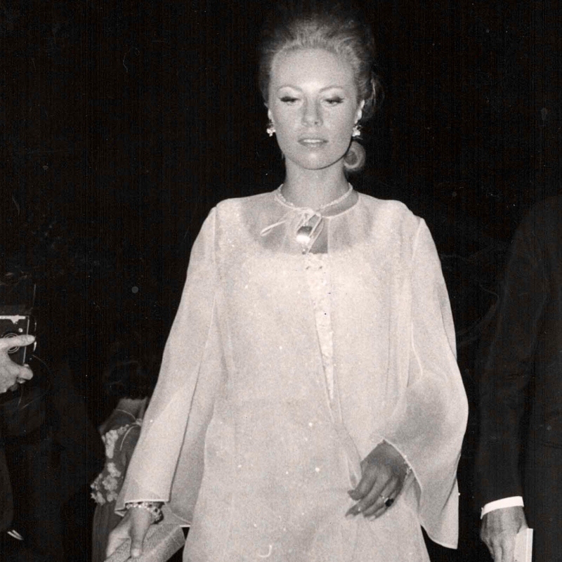 Frau in eleganter, weißer Abendgarderobe mit langen Ärmeln, umgeben von Menschen und Kameras, 1960er Jahre.