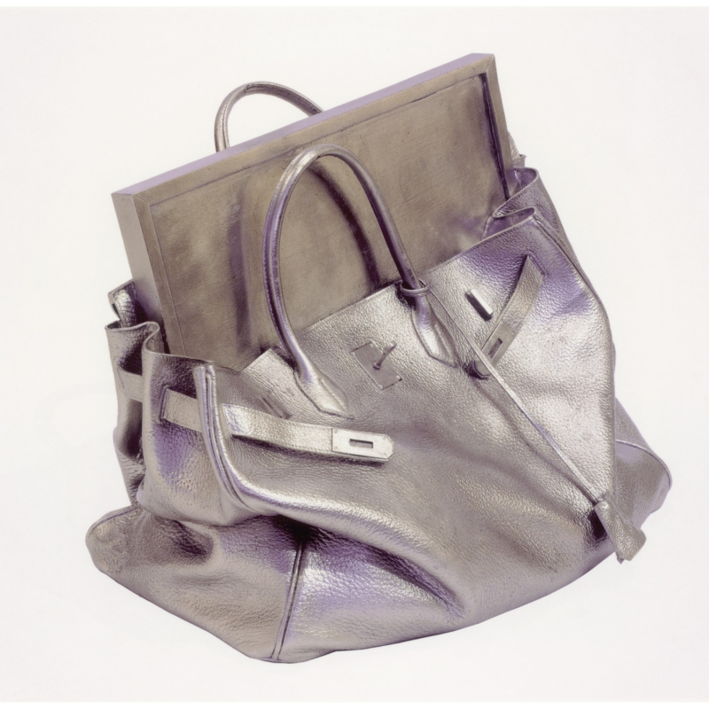 Silberne Handtasche mit einem rechteckigen, silbernen Objekt darin, auf weißem Hintergrund.